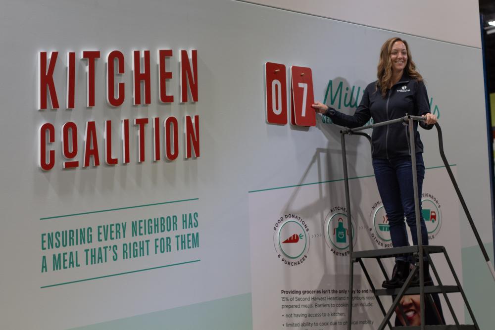 Woman on ladder smiles while hanging up number 7 on Kitchen Coalition mural.