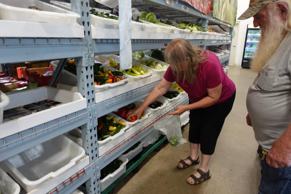 Woman in pink shirt picking out produce from a shelf of bins