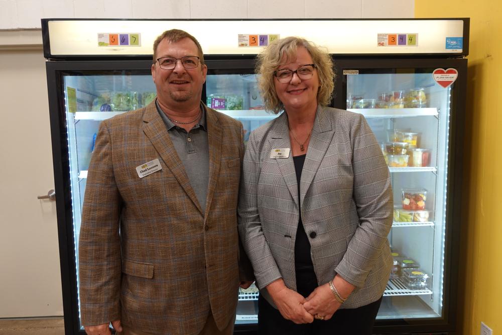 Two people wearing blazers and name tags standing in front of a cooler