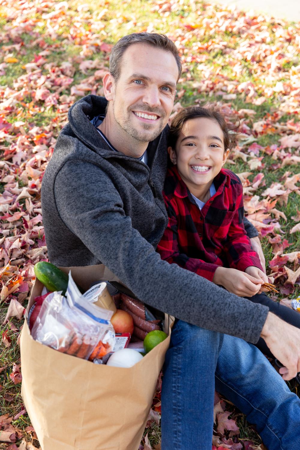 Give to the Max Day 2 people pictured sitting outside on grass covered with autumn leaves - one adult one child