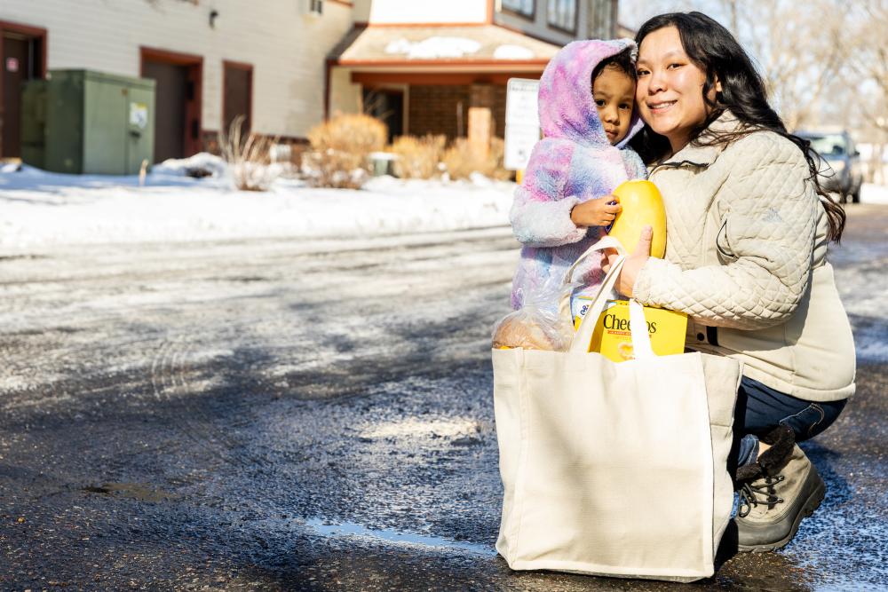 Adult with child outside in wintery weather with grocery bag