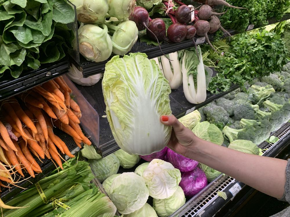 A hand picks out a napa cabbage from a grocery store