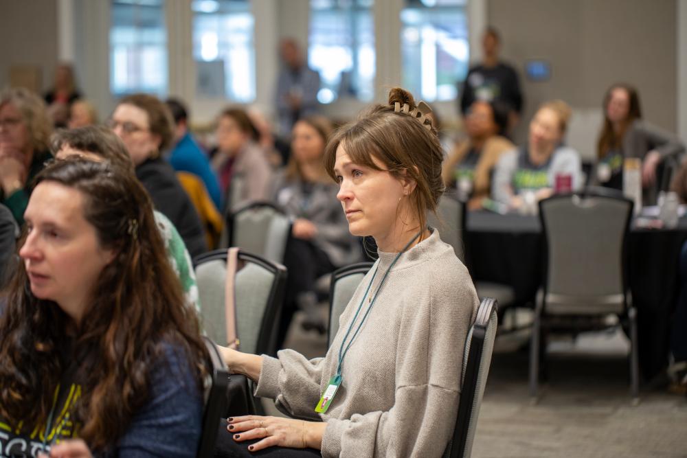 A seated woman listening to a presenter during a breakout session