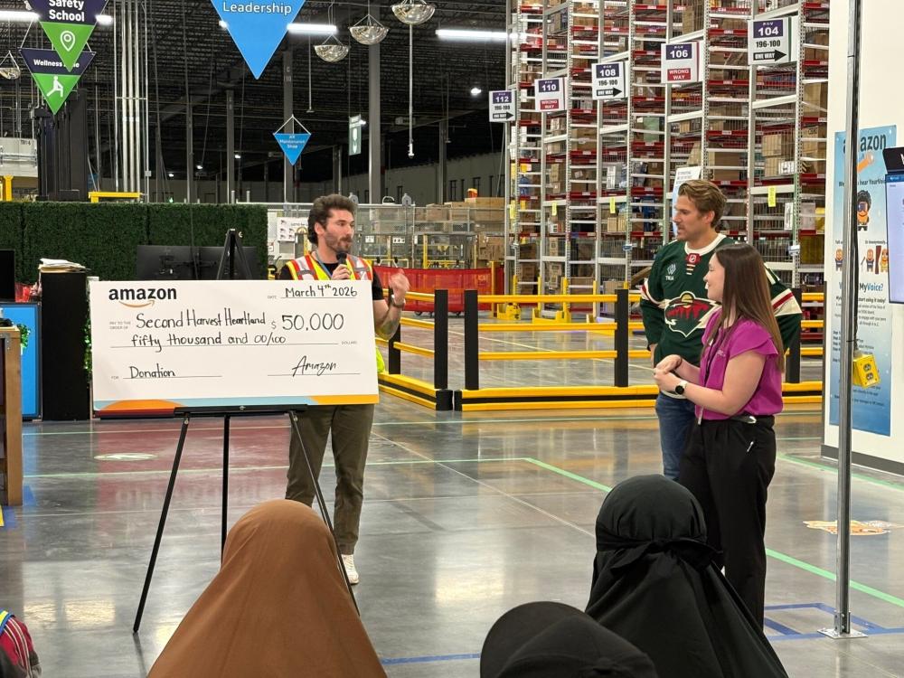 A large check is displayed by a person talking to a crowd in a warehouse