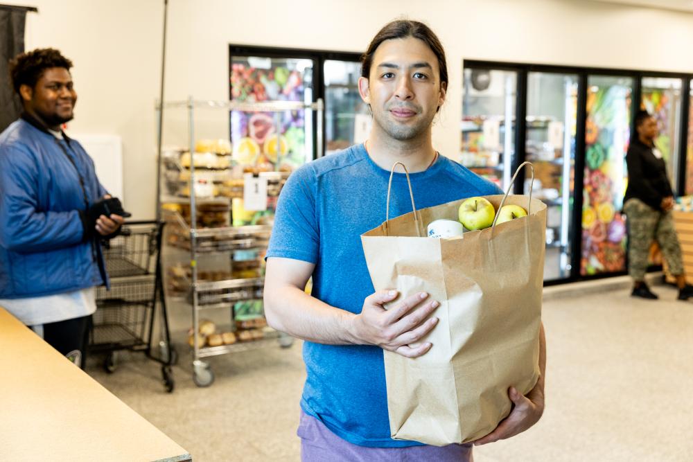Man standing in food shelf with paper bag of grocery items