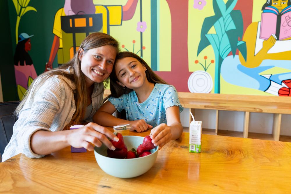 Adult woman with a child sitting at a table eating strawberries out of a bowl