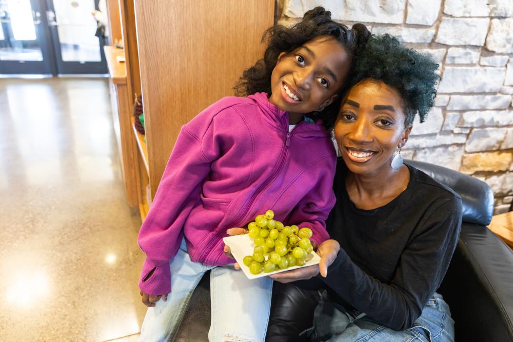 Mother and daughter smiling while holding a bunch of green grapes