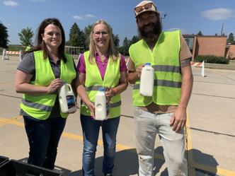Three people standing holding gallon milk bottles