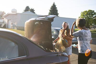 Two women load food into the trunk of a car