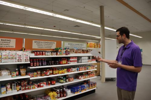 A food shelf worker in front of shelves of canned goods.