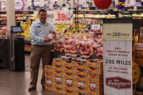 A grocer stands with a display of local apples