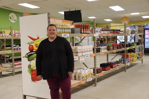 A food shelf worker in front of shelves of canned goods.