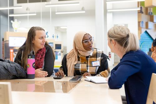 Three women at a table are having a conversation