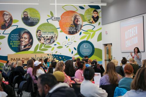 A group of people in a brightly colored room listen to a speaker