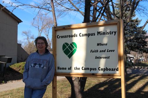 A woman in a sweatshirt standing outside of a food pantry sign