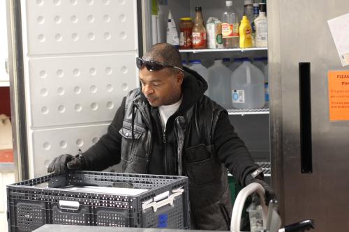 A man in a black jacket loading meals into a refridgerator