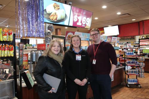 Two women and a man pose for a photo in front of a hot bar at a Kwik Trip