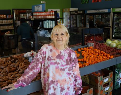 A woman in a floral pattern shirt poses in front of oranges