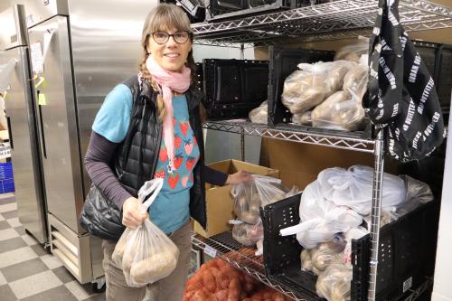 A volunteer takes potatoes in bags off of a shelf