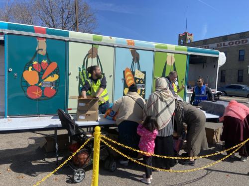 Families picking up food at a mobile distribution Food shelf visitors picking up food in front of colorful mobile distribution trailer.