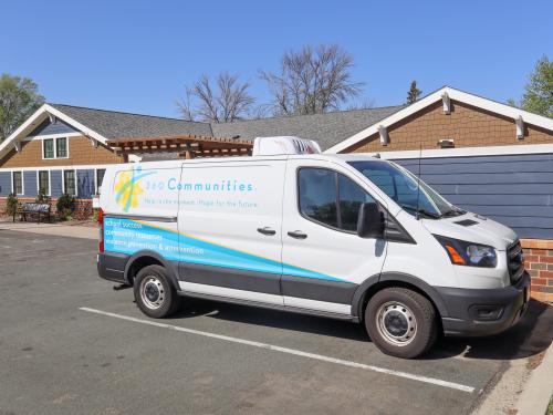 360 Communities Van A white and blue van with 360 Communities on the side parked near a low brown building.