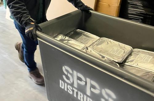 SPPS cart of donated meals A gray cart labeled "SPPS" being pushed by a person in dark clothing full of foil-covered pans of food