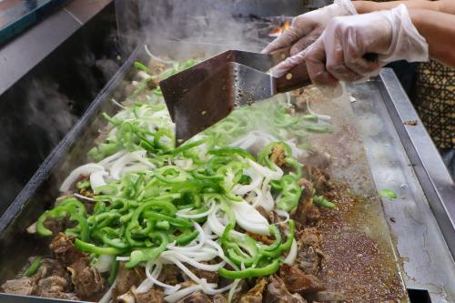 Goat meat and peppers are prepared on a skillet