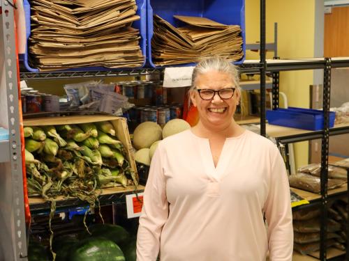 Lisa standing in 360 Communities food shelf Lisa wearing a big smile, glasses, and a white shirt standing in 360 Communities food shelf in front of a rack of corn on the cob