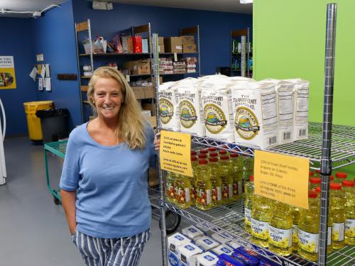St. Peter Area Food Shelf Coordinator Jodi Woman in blue shirt standing by shelves of flour and oil in a food shelf