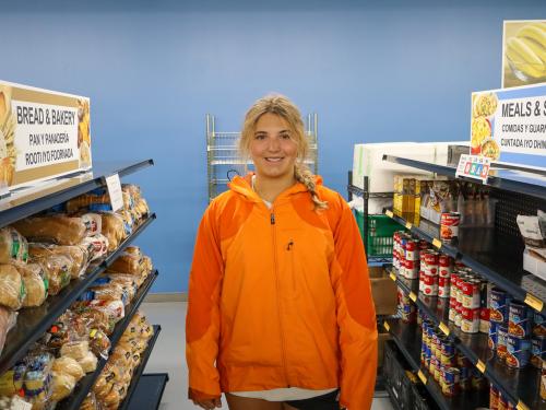 A young woman in an orange jacket in a food market aisle