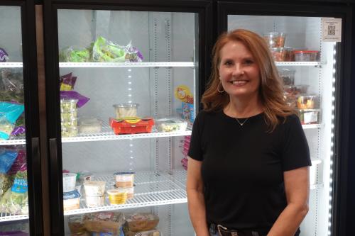 Woman in black shirt smiling in front of a cooler of food.