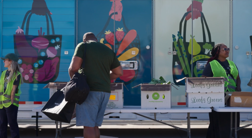 Person picking up produce in front of colorful mobile trailer