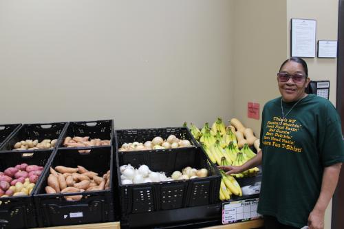 A woman smiles at the camera next to a display of produce