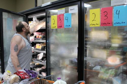 A man reaches in a grocery cooler next to a full shopping cart