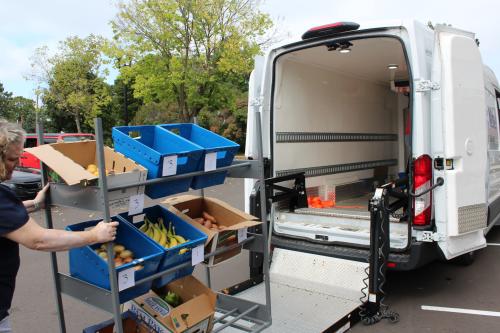An open van with a person removing a rack of produce