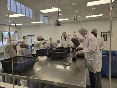 Volunteers in white coats and hairnets packing chocolate cereal in bags