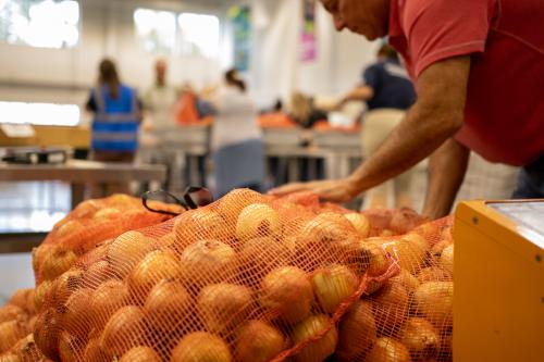 A volunteer stacks red mesh bags of onions in the Volunteer Center