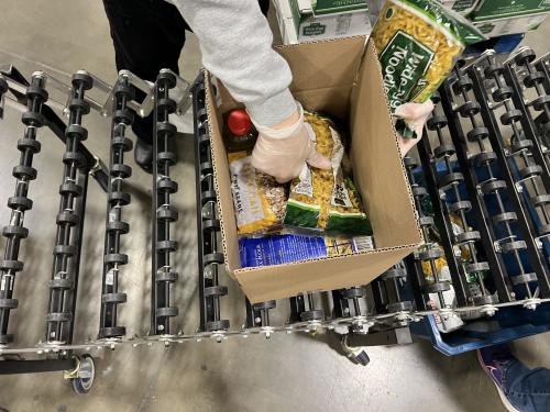A volunteer's hand putting a bag of noodles in a full emergency box.