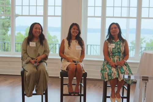 Three women sitting in chairs smiling in front of big windows