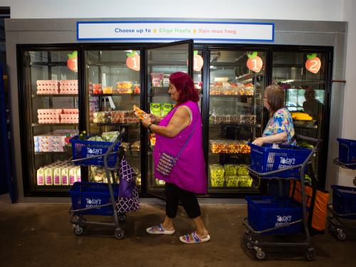 Two people with shopping carts in front of a grocery store style cooler